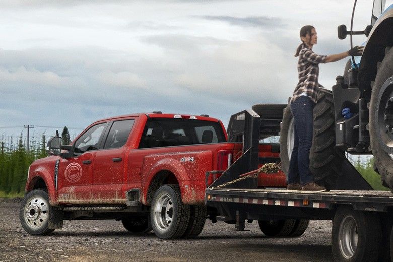 A woman loading a tractor onto a trailer pulled by a red Ford truck